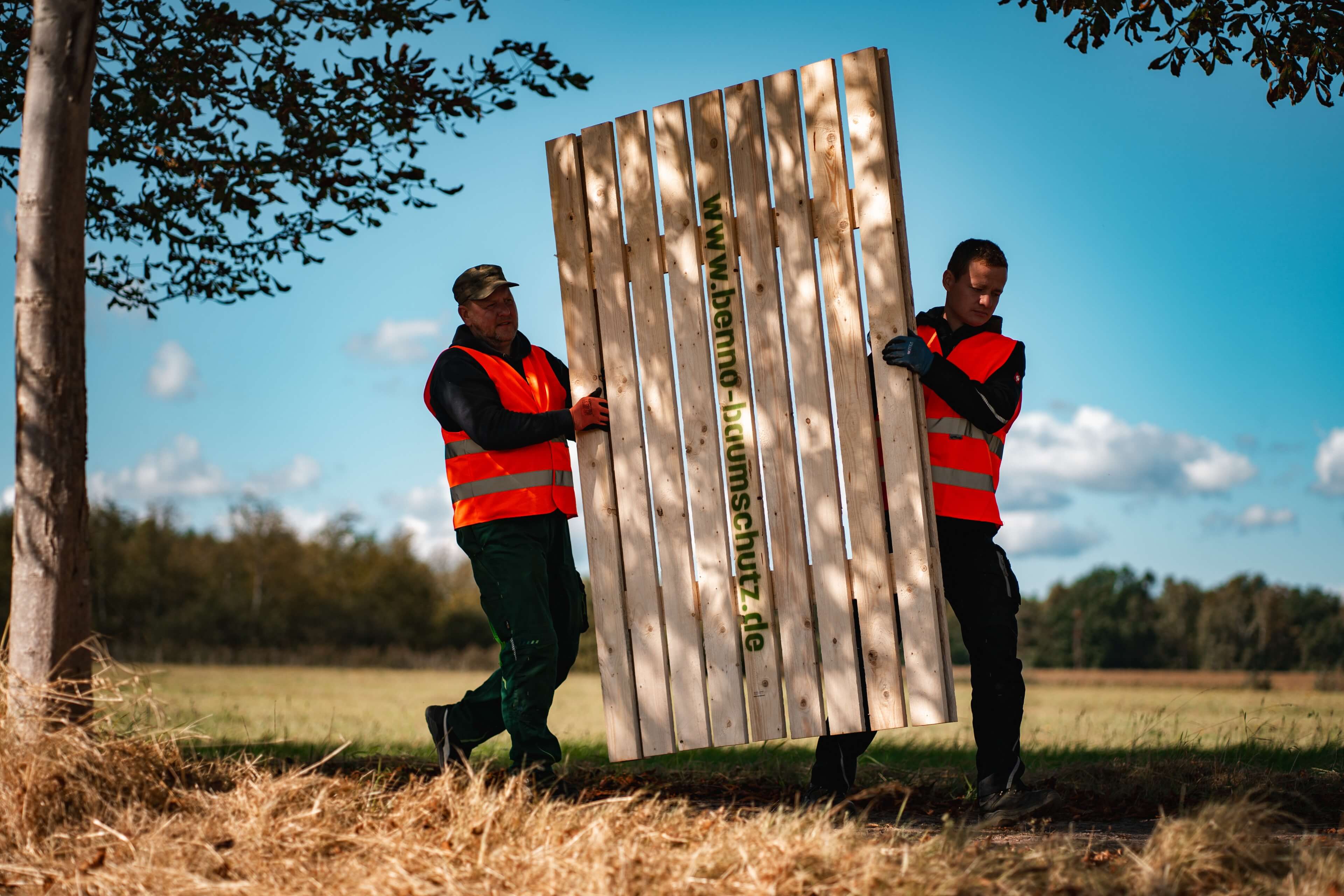 Männer heben ein Holzelement für den Baumschutz im Freien